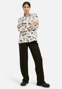 White button-up shirt with black patterns, paired with black wide-leg pants and chunky black shoes. Smooth fabric, relaxed fit, long sleeves.