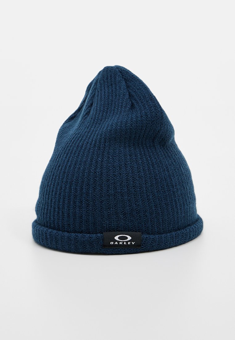 Beanie lavorato a maglia blu navy con bordo ripiegato e patch del logo Oakley nero sulla parte frontale, posizionato su uno sfondo bianco.
