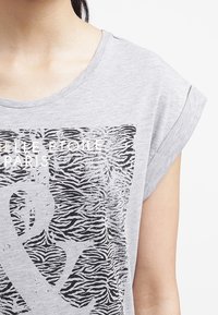 Harmaa lyhythihainen t-paita, jossa on musta seepra-kuviointi ja valkoinen teksti "ELLE ÉTOILE PARIS." Pehmeää puuvillamateriaalia.