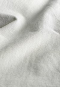 Szary materiał o drobnej prążkowanej fakturze, ukazujący miękkie fałdy i subtelny połysk. Lekko pognieciona powierzchnia z delikatnymi, równymi liniami.