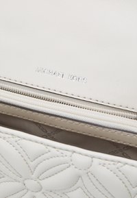 Borsa Michael Kors in pelle bianca con trapuntatura floreale, zip a vista e rivestimento interno con logo.