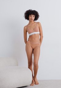 Calvin Klein kailīga krūšturi un bikini komplekts, kas iezīmējas ar viendabīgu krāsu, mīkstu materiālu un baltu elastīgu joslu ar logo akcentu.