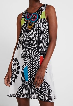 Sukienka bez rękawów z wyrazistymi czarno-białymi geometrycznymi wzorami, kolorowymi abstrakcyjnymi detalami oraz okrągłym dekoltem na ciemnoskórej osobie.