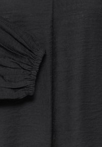 Tissu noir avec un gros plan sur un poignet froncé, élastique et une couture verticale visible sur tissu lisse.