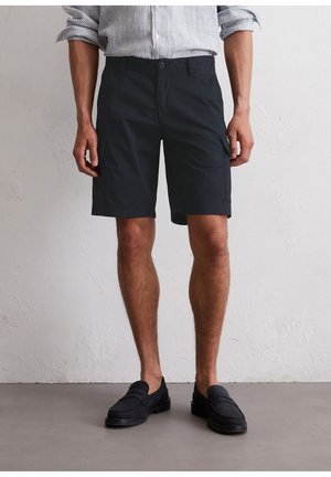 Pantalones cortos de hombre en azul marino, hechos de algodón, con un corte recto, dos bolsillos laterales y cierre de botón. Combinados con mocasines negros.