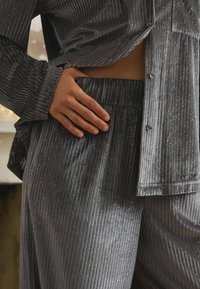 Šedý sametový domácí outfit se svislým jemným žebrováním, který obsahuje diskrétní glitrové detaily a volný střih. Košile na knoflíky a elastický pas.