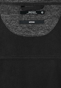 Black fleece fabric with a textured grey inner collar. Label reads "INDIGO," "CARRY OUR PASSION," and size "MEDIUM" in white text.