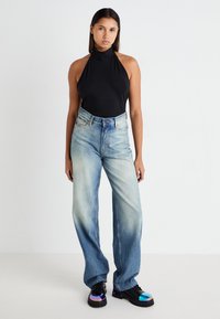 Top preto com halter, jeans de perna larga de cintura alta azul-claro e sapatos pretos robustos com detalhes iridescentes. Fundo plain.