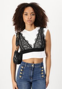Črna čipkastá bralette s valovitimi robovi na beli kratki majici, v kombinaciji z modrimi visokimi-nizkimi jeans hlačami z zlatimi gumbi. Črna prešita torbica.