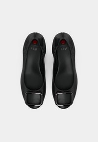 Black ballet flats made of smooth material, featuring a square metallic accent on the toe and subtle elastic detailing around the opening.