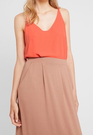 Haut rouge sans manches avec un col en V, associé à une jupe beige longueur genou avec des plis et une texture douce.