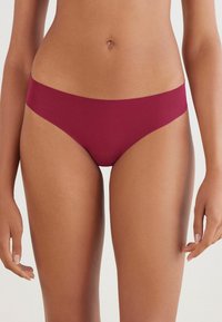 Burgundowe bikini o gładkiej fakturze, niskim stanie, minimalnym kryciu i braku widocznych szwów, co zapewnia bezszwowy wygląd.
