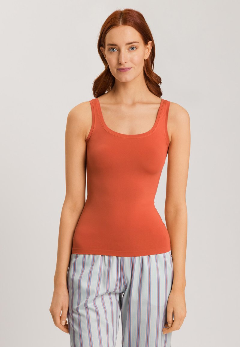 Top a maniche corte aderente in arancione ruggine, realizzato in tessuto elasticizzato. Texture morbida, spalline larghe e scollatura arrotondata, abbinato a pantaloni a righe.