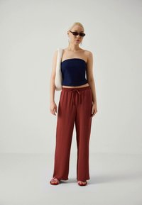 Navy strapless top, loose red trousers with drawstring, and pink sandals. Model holds white bag; wears dark sunglasses and earrings.