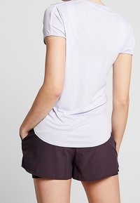 Ljuslila kortärmad t-shirt med rundad nederkant, i kombination med mörklila träningsshorts. Materialet verkar lätt och ventilerande.