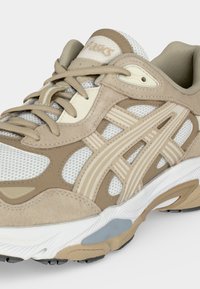 Μπεζ και λευκό αθλητικό παπούτσι με ύφασμα δίχτυ, επενδύσεις από σουέτ, δέσιμο με κορδόνια μπροστά και γεωμετρική σόλα.