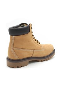 Stivale da lavoro in pelle tan con lacci, colletto imbottito scuro e suola in gomma spessa, angolato per mostrare il lato esterno e il retro.