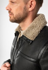 Zwarte leren jack met beige faux shearling kraag, ritssluiting en borstzak. Gladde textuur met subtiele nerfdetails.