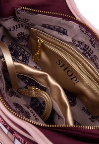 Innenseite einer kastanienbraunen Tasche mit goldenen Akzenten, ausgestattet mit einer Reißverschlusstasche und einem gemusterten Innenfutter. Enthält einen herzförmigen Schlüsselanhänger im Inneren.