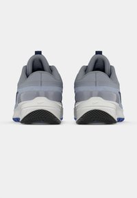 Grå atletiska skor med en texturerad mesh-överdel och genomskinliga detaljer. Har en vit mellansula och en svart gummisula med blå accenter.