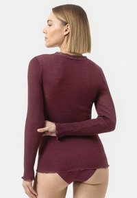 T-shirt à manches longues en rib en bordeaux foncé avec un bord en dentelle festonnée à l'encolure et à l'ourlet. Silhouette cintrée et texture douce.