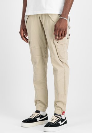 Pantalones cargo beige con múltiples bolsillos, textura suave, corte ajustado y detalles de costura, combinados con zapatillas negras y blancas.
