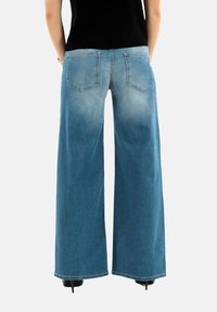 Pantalons en jean à jambes larges de couleur bleu clair avec une texture décolorée, dotés de deux poches arrière et d'une taille ajustée. Des chaussures à talons sont visibles sous l'ourlet.