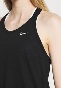 Černý sportovní top bez rukávů vyrobený z hladké tkaniny, s designem na zádech ve tvaru jezdce, bílým logem Nike a vrstveným vzhledem s bílým vnitřním topem.
