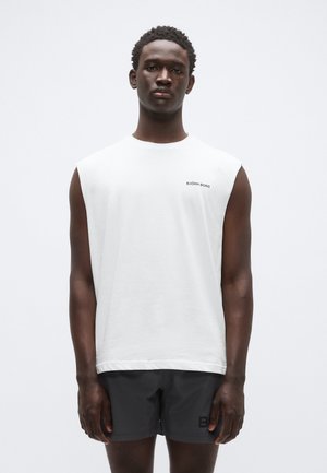 Witte mouwloze t-shirt met een ronde halslijn en zwart "BJÖRN BORG" logo. Gecombineerd met donkergrijze korte broek. Glad katoenen stof, comfortabele pasvorm.