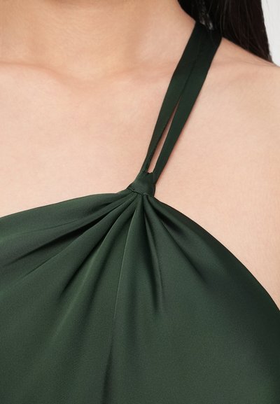 Top verde închis tip halter cu un detaliu înnodato la decolteu, realizat dintr-un material neted, ușor și cu bretele subțiri pentru un aspect fixat.