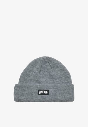 Hallid hall villane beanie, mis on valmistatud pehmest kangast, millel on rullitud äär ja must ristkülikukujuline silt tekstiga "UNFAIR". Sile tekstuur.