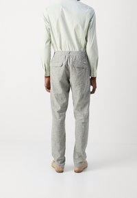 Pantalons gris texturé avec une taille élastique, poches arrière, associés à une chemise à manches longues vert clair et des chaussures de couleur claire.