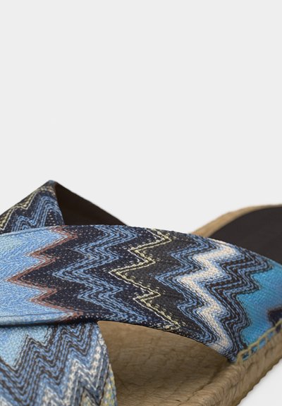 Περιπατητική σάνδαλος με πλεγμένα λουριά σε ζιγκ-ζαγκ μοτίβο σε μπλε, μαύρο και λευκό, πάνω σε υφασμένο ταμπά πέλμα και μαύρη εσωτερική σόλα.