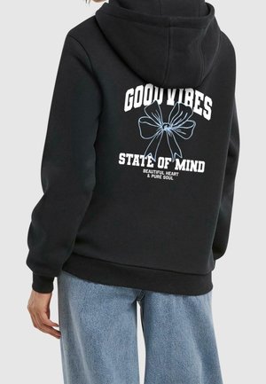 Czarna bluza z kapturem noszona przez osobę, z białym napisem „GOOD VIBES STATE OF MIND” i niebieskim konturkiem kokardy na plecach.