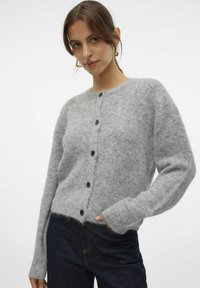 Gilet gris en tricot fabriqué en tissu doux et duveteux, avec un col rond, des manches longues et des boutons noirs sur le devant.