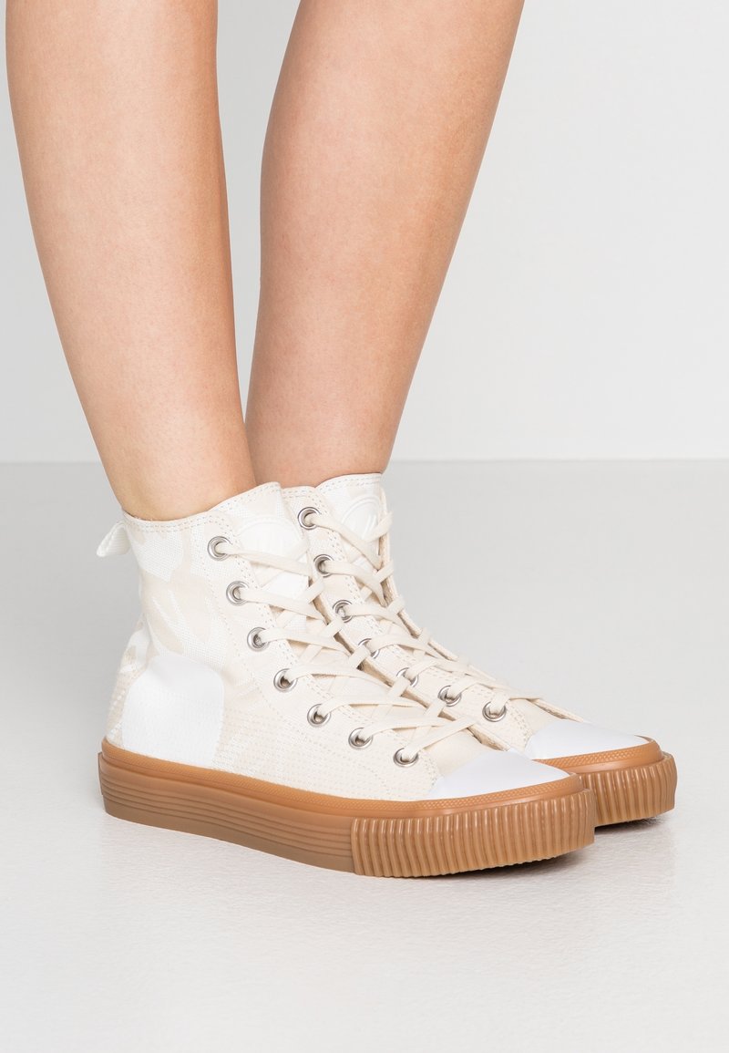 Höga sneakers i off-white canvas med en strukturerad yta, gummisula och vit tåhuvud; har metalldetaljer och snörningsdesign.