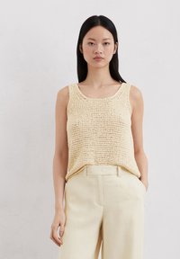 Lichtgele gebreide tanktop met een brede ronde hals, voorzien van een textuurpatroon. Gecombineerd met crèmekleurige casual broek.