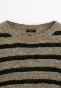 Beżowy sweter w paski z czarnymi poziomymi paskami, z okrągłym dekoltem i miękką, puszystą teksturą. Metka widoczna wewnątrz kołnierza.