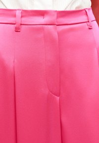 Φούξια παντελόνια ψηλόμεσα με θηλιές για ζώνη, συνδυασμένα με λευκή μπλούζα, εστίαση στη μέση και την περιοχή των γοφών.