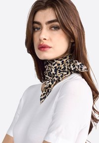 Bufanda de seda con estampado de leopardo atada al cuello, con tonos de beige y negro, combinada con una sencilla blusa blanca de manga corta.
