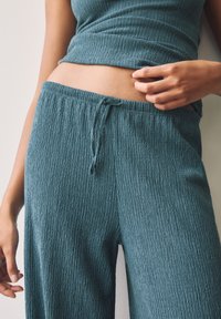 Turkos, texturerad klädset med en figursydd topp och lösa byxor. Byxorna har resår i midjan och dragsko-detalj.