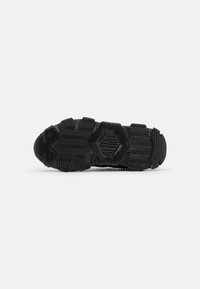 Black sneaker sole with textured rubber, featuring zigzag patterns and raised branding. Durable design for traction and stability.