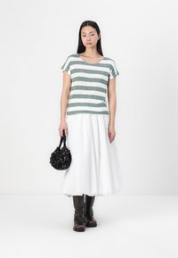 Stribet grøn og hvid kortærmet top, hvid fuld nederdel, ankellange brune støvler og en sort dekorativ taske med blomstrede detaljer.