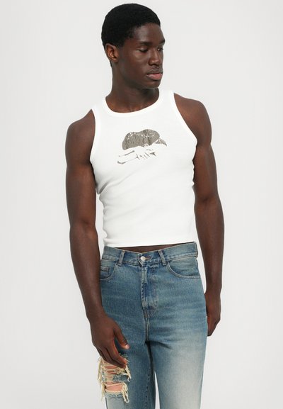 Weißes Tanktop mit einem grafischen Druck auf der Brust, kombiniert mit ausgewaschenen blauen Röhrenjeans, die einen lässigen, entspannten Schnitt betonen.