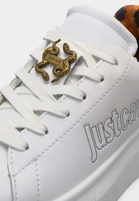 Λευκό sneaker Just Cavalli με λευκά κορδόνια, χρυσό διακοσμητικό σε σχήμα φιδιού στα κορδόνια και λεπτομέρεια με εσωτερική επένδυση σε λεοπάρ σχέδιο.