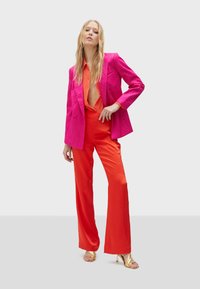 Fuksia blejzer s teksturiranim završetkom, narančasta satenasta košulja i crvene satenaste široke hlače. Zlatne sandale s remenčićima upotpunjuju outfita.