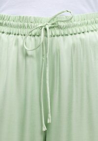 Φωτεινά πράσινο παντελόνι με ελαστική μέση και δεμένο κορδόνι σε φόντο λευκού υφάσματος.