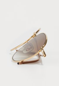 Ochelari de soare aviator aurii cu lentile de nuanță căprui, având un cadru subțire din metal și brațe curbe. Design ușor și elegant.