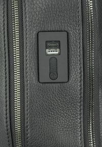 Sac en cuir texturé noir avec une fermeture éclair en métal. Comprend un panneau de port de charge noir avec des connecteurs USB et USB-C.