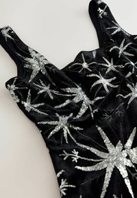 Fekete bársony, ujjatlan felső, ezüst flitteres csillagvirág mintákkal, amelyek szétszórva vannak az anyagon, világos háttér előtt.